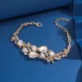 Raffinato bracciale in lega dorata con strass e cristalli scintillanti, provvisto di catenina. - Champagne