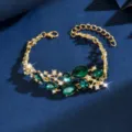 Primo piano di bracciale in lega dorata con cristalli verde smeraldo e strass luminosi. - Oro Verde
