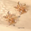 Primo piano di eleganti orecchini a forma di fiore dorato 3D con dettagli metallici raffinati. - Stile Fiore Tridimensionale (80118702) / Oro