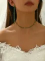 Close-up shot of a glamorous green rhinestone choker necklace and long earrings set on model. - Gold Green Set