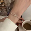 Close-up of a silver double layer knot bracelet worn on wrist, elegant jewelry detail shot. - Knotted Bangle Bracelets