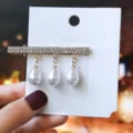 Gros plan détaillé d'une barrette à strass élégante avec trois perles sur carton blanc. - S43-1# Pinces à bec de canard à strass avec pendentifs en perles