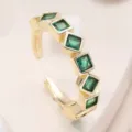 Gros plan sur la bague ouverte dorée ornée de pierres de zircone vert carré étincelantes. - Style E