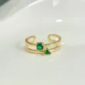 Gros plan sur une bague double en or avec des oxydes de zirconium verts ronds et triangles. - Style F