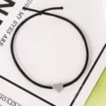 Primer plano de coletero negro elástico con un dije de corazón gris mate, detalle. - 7# Coleteros grises con corazón pequeño