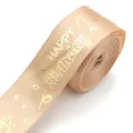 Close-up detail of the champagne gold satin ribbon with metallic birthday stamping pattern. - Khaki