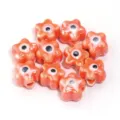 Close-up detailweergave van oranje keramische bloemkralen met boze oog motief voor DIY sieraden. - 10 Stuks/Pak / Oranjegeel