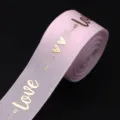 Pink polyester grosgrain ribbon featuring metallic gold love and heart print detail close up. - Light Pink