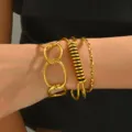 Primo piano di un set di bracciali in metallo dorato multistrato con maglie geometriche. - Set di 3 / Oro