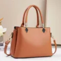 Detailed view of the brown leather commuter handbag showing golden hardware and handle design. - Earthy Yellow
