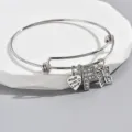 Detailed shot of silver adjustable charm bracelet with rhinestone letter F heart butterfly. - Style F