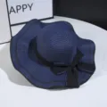 Close up of navy blue straw hat with black bow and wavy brim, perfect for summer sun protection. - Navy Blue