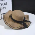Straw hat detail showcasing the wide wavy brim and elegant black bow decoration for summer. - Khaki