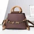 Vista dettagliata della borsa marrone elegante con manico in legno e catena. - Caffè