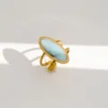 Detalle en primer plano de un anillo geométrico dorado minimalista con una piedra azul clara. - Estilo Geométrico Ovalado Azul Claro
