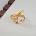 Close-up of golden open stainless steel ring featuring a sparkling square cubic zirconia stone. - Square Cut Stone Style / Gold