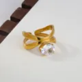 Close-up of stainless steel cross open ring with clear cubic zirconia crystal detail. - Crossed Lines Style / Gold