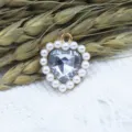 Close-up view of a sparkly heart-shaped crystal pendant framed by classic faux pearls. - White