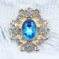 Detailed close-up of a gold-tone alloy rhinestone flower button with a blue center gem. - Lake Blue