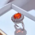 Primo piano di un anello con pietra preziosa arancione brillante e doppio alone in argento. - Anello / Rosso