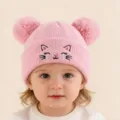 Détail de bonnet tricoté rose avec visage de chat brodé mignon et pompons doubles duveteux. - Rose