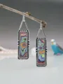 Primo piano di orecchini pendenti colorati in fordite stile boho pendono da un ramo d'albero. - Stile Gancio Rettangolare (11887)