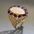 Dettaglio di un anello vintage dorato con un grande opale iridescente e pietre viola luminose. - Taglia 6 / Oro Viola