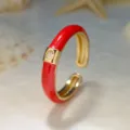 Primo piano di un anello aperto dorato con smalto rosso brillante e uno zircone luminoso. - Aperto Regolabile / Rosso