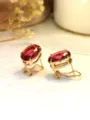 Primo piano dettagliato di eleganti orecchini dorati con pietre preziose rosse ovali. - Oro KC Rosso