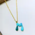 Primo piano di una collana con ciondolo alfabeto colorato con dettagli in smalto raffinati. - Taglia M