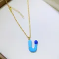 Dettaglio di una collana con ciondolo lettera capsula stile dopamina color oro chic. - Lettera U