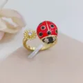 Primo piano dettagliato dell'anello aperto dorato con coccinella smaltata rossa e fiore. - Coccinella