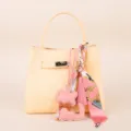 Detailed close-up shot of light yellow handbag with cute pink cat charm and silk scarf. - Pink Tassel Scarf and Pink Kitten