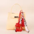 Yellow leather handbag detail featuring a stylish red cat keychain and silk scarf tassel charm. - Red Tassel Scarf & Red Kitten