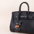 Nahaufnahme der schwarzen Leder-Henkeltasche mit süßem Schleife-Tieranhänger und Metallbeschlägen. - Kleiner Fuchs (BHT06) / Schwarz