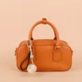 Close-up detail shot of a stylish orange leather handbag showcasing a cute hand-woven ball charm. - SJQ22 Green - Gold Buckle / Green