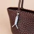 Detailed view of brown leather woven handbag featuring a chic light blue braided keychain charm. - Light Blue