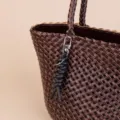 Detailed view of dark brown woven leather tote bag with stylish black rope keychain accessory. - Black