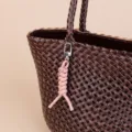 Close-up detail of a dark brown woven leather handbag paired with a cute pink keychain strap. - Pink