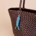 Detailed close-up view of a blue braided leather keychain hanging on a brown woven bag. - Blue