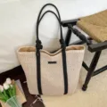 Detail shot of the woven paper rope tote bag with black handles in a cozy room setting. - Off White