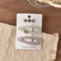 Primo piano dettagliato di mollette per capelli floreali e a quadri su una carta. - Clip BB a Goccia d'Acqua a Quadri Marroni e Fiori Verdi (FJ911) / 2 Pezzi/Set