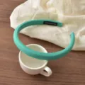 Detail view of a stylish turquoise diagonal stripe headband resting on a white cup and cloth. - 9# Lake Green