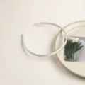 Gros plan d'un fin serre-tête en satin argenté, design minimaliste pour coiffure quotidienne. - Blanc
