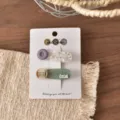Primo piano dettaglio di graziose mollette per capelli a bottone su carta con sfondo tessuto. - Fermaglio a Becco d'Anatra a Goccia d'Acqua con Bottone Patchwork Viola (FJ911)