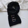 Close-up detail of a black knitted scarf featuring cute embroidered dachshund dogs and text. - Scarf / Black