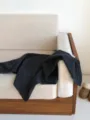 Dark grey knitted wool shawl detail view, cozy home scene showcasing soft fabric texture. - Gray
