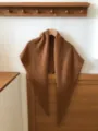 Detailed close-up view of the cozy brown wool blend triangular scarf on wooden hook. - Caramel color