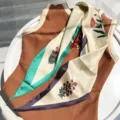 Detailed view of the elegant geometric floral silk scarf draped on a brown vest, stylish accent. - 115x35cm / Green