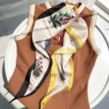 Floral print silk scarf detail, elegant small neckerchief draped on brown top, close-up shot. - 115x35cm / Yellow